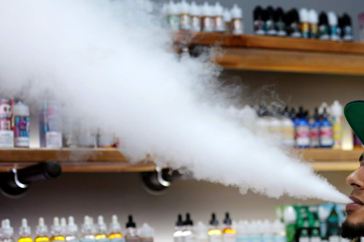 FILE - In this Tuesday, Sept. 3, 2019 file photo, a salesman at a vape shop exhales while using an e-cigarette in Maine.