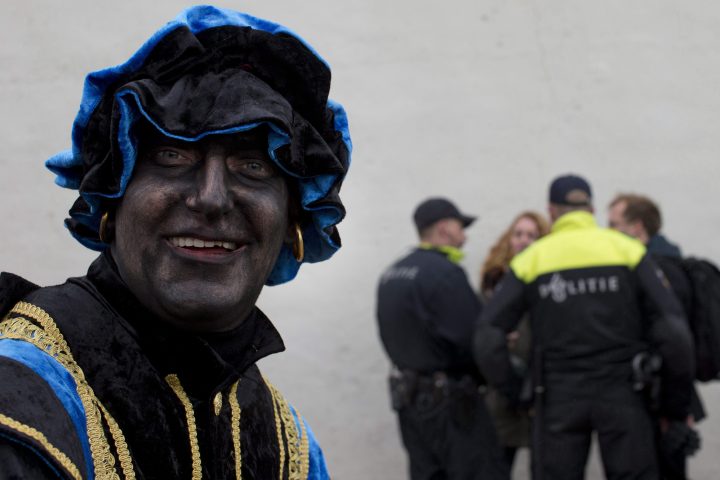 A Black Pete takes part in a far-right demonstration in a closed off area while police officers question two people, rear, during the arrival of Sinterklaas, the Dutch Saint Nicholas, in Maassluis, Netherlands, Saturday, Nov. 12, 2016.
