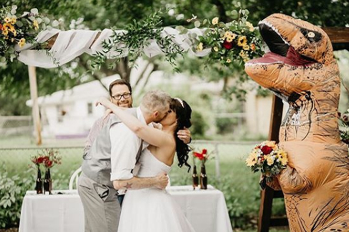 Joby and Deanna Adams share a kiss while Christina Meador stands nearby in a T. rex costume on Aug. 10, 2019, in Omaha, Neb.