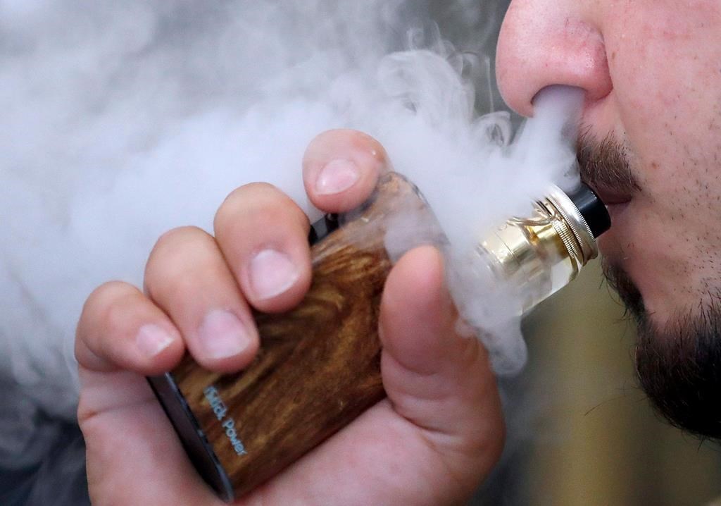 FILE - In this Friday, Aug. 17, 2018 file photo, a man breathes vapes from an e-cigarette at a vape shop in London.