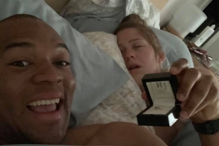 Edi Okoro, left, holds up an engagement ring while his girlfriend Cally Read sleeps next to him.