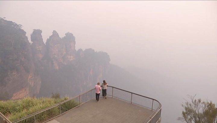 In this image made from video, two people watch from a look out of smoke from wildfire, Monday, Dec. 23, 2019, in the Blue Mountains, New South Wales, Australia.