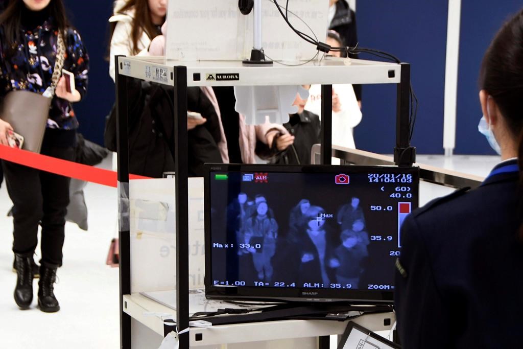 In this Jan. 16, 2020, photo, travelers from China's Wuhan go through body temperature scanners at Narita airport in Narita, near Tokyo. A fourth person has died in an outbreak of a new coronavirus in China, authorities said Tuesday, Jan. 21, 2020, as more places stepped up medical screening of travelers from the country as it enters its busiest travel period. (Kyodo News via AP).