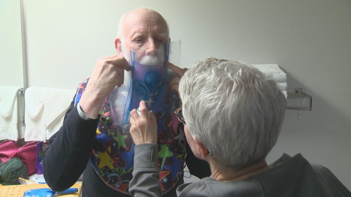 Madsen\’s wife, Judy, spray paints Team Quebec\’s fleur-de-lis logo onto his beard.