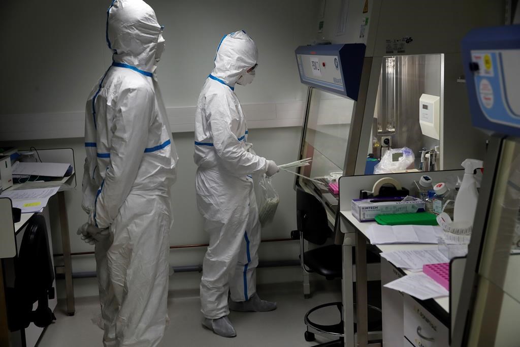 French lab scientists in hazmat gear inserting liquid in test tube manipulate potentially infected patient samples at Pasteur Institute in Paris, Thursday, Feb. 6, 2020. Scientists at the Pasteur Institute developed and shared a quick test for the new virus that is spreading worldwide, and are using genetic information about the coronavirus to develop a potential vaccine and treatments.
