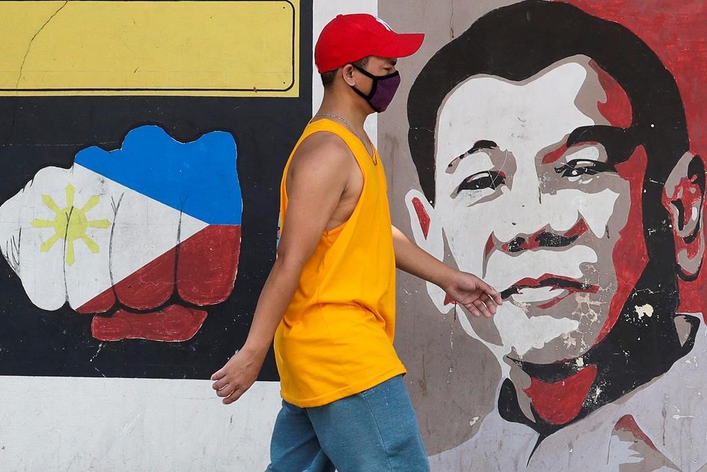 A man wearing a protective mask walks past an image of Philippine President Rodrigo Duterte in Manila, Philippines on Friday March 20, 2020.