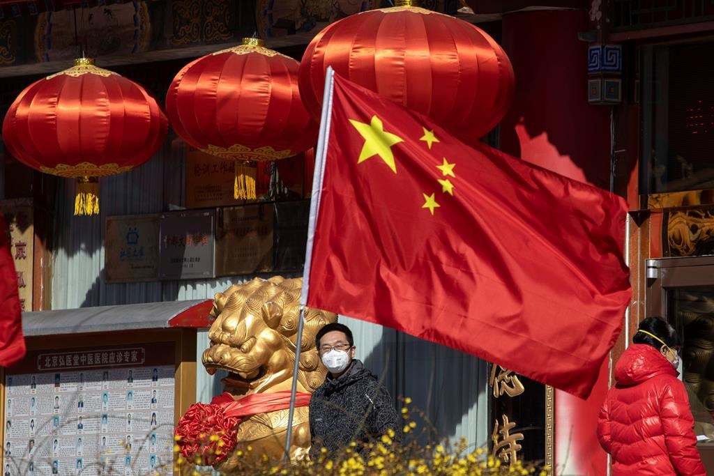 A masked man looks out near a national flag outside a traditional medicine hospital in Beijing on Tuesday, March 3, 2020.