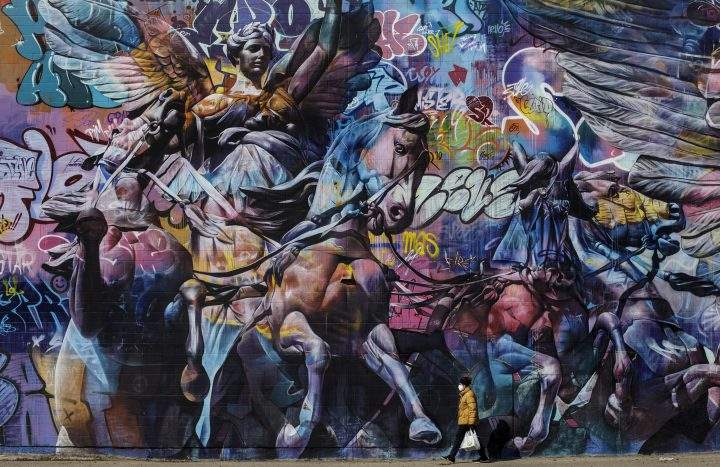 A person carrying groceries and wearing a mask walks past a mural in Edmonton during the COVID-19 pandemic on Saturday, April 11, 2020.