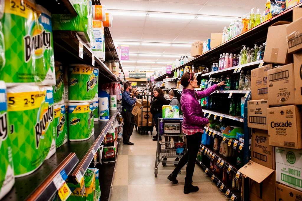 In this March 12, 2020, file photo, customers shop for cleaning products as market employees restock shelves.