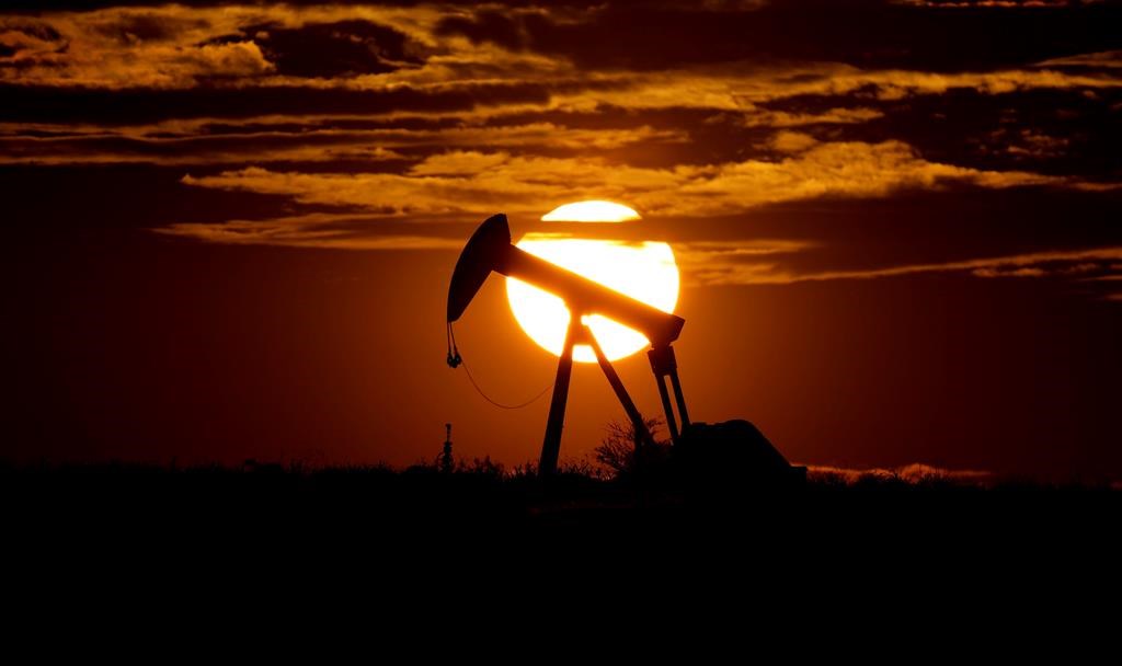 The sun sets behind an idle pump jack. 