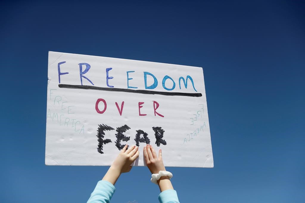 FILE - In this April 21, 2020, file photo a person holds a sign while gathering with others to protest stay-at-home orders put into place due to the COVID-19 outbreak outside the Missouri Capitol in Jefferson City, Mo. Amid pockets of attention-grabbing protests, a new survey finds Americans remain overwhelming in favor of stay-at-home orders and other efforts to slow the spread of coronavirus. (AP Photo/Jeff Roberson, File).