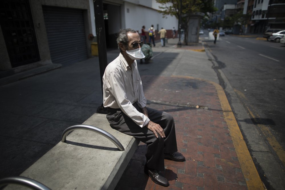 An elderly man wearing a mask to avoid the spread of the new coronavirus suns himself on a bench in Caracas, Venezuela, Sunday, May 24, 2020. 