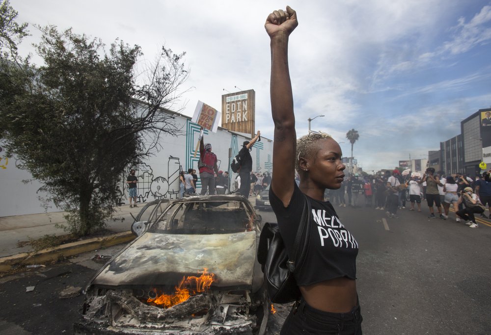 A protester poses for photos next to a burning police vehicle in Los Angeles, Saturday, May 30, 2020, during a demonstration over the death of George Floyd. a black man who was killed in police custody in Minneapolis on May 25.