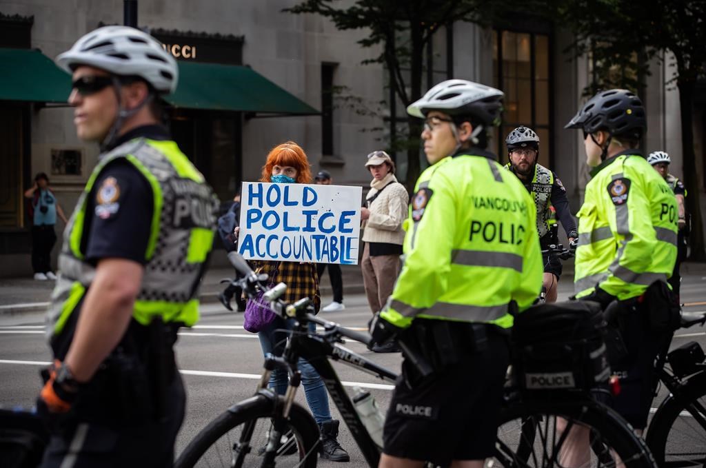 A woman holds a sign reading "Hold Police Accountable" near police officers watching as thousands of people gather for a peaceful demonstration in support of George Floyd and Regis Korchinski-Paquet and protest against racism, injustice and police brutality, in Vancouver, on Sunday, May 31, 2020.