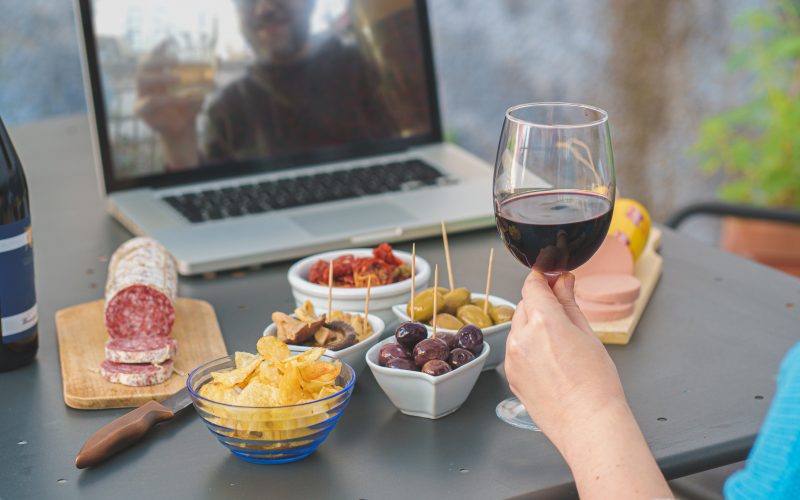 Two people share a drink and some snacks via a virtual meeting. 