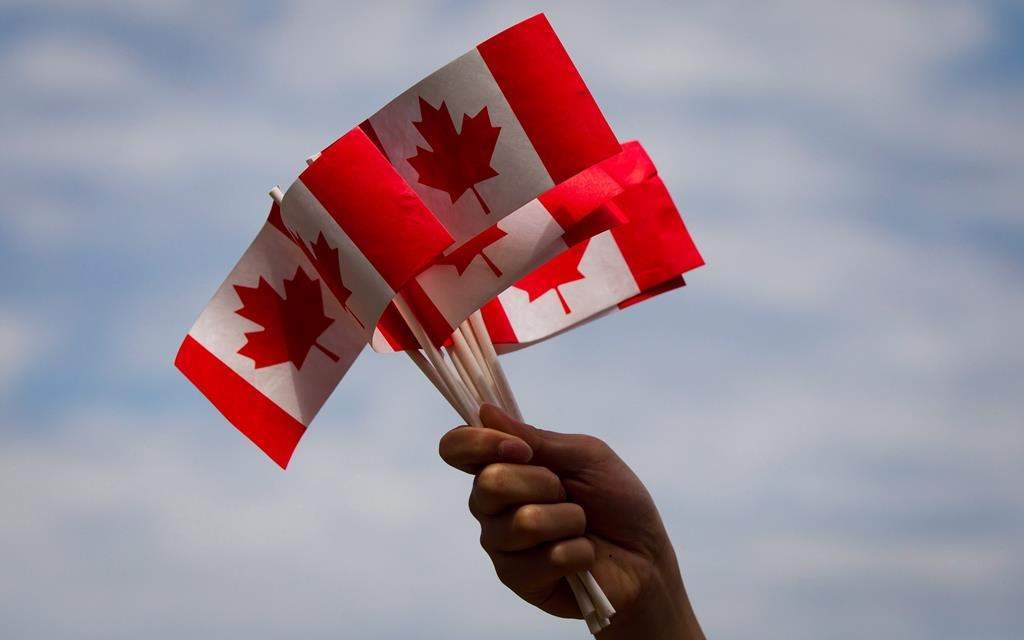 A volunteer waves Canadian flags while handing them out to people during Canada Day festivities in Vancouver, B.C., on Monday, July 1, 2013. COVID-19 means the true north is not entirely free this Canada Day, but a new survey suggests that's not going to change how many people mark the holiday. THE CANADIAN PRESS/Darryl Dyck.