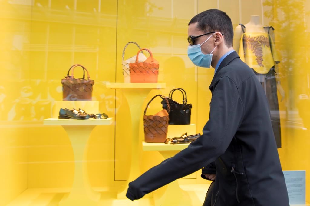 A pedestrian wears a protective face mask as they walk past a re-opened shop in downtown Vancouver, Tuesday, June 2, 2020.