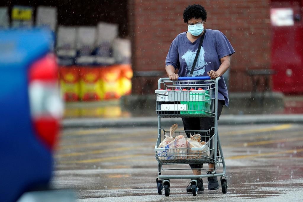 A shopper wears a mask as she pushes her grocery cart in the rain Thursday, June 25, 2020.