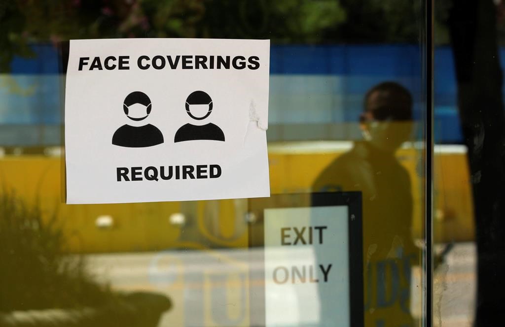 A man wearing mask to protect against the spread of COVID-19 is reflected next to a sign requiring face coverings at a business in San Antonio, Wednesday, June 24, 2020.