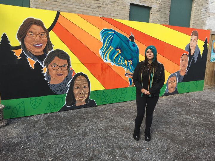 Tristen Jenni Sanderson stands in front of the large mural she created at the Boyle Street Community Services centre in downtown Edmonton.