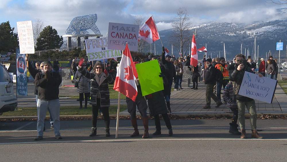 Demonstrators holding signs and Canadian flags at a rally in downtown Kelowna on Saturday, Dec. 12, 2020.