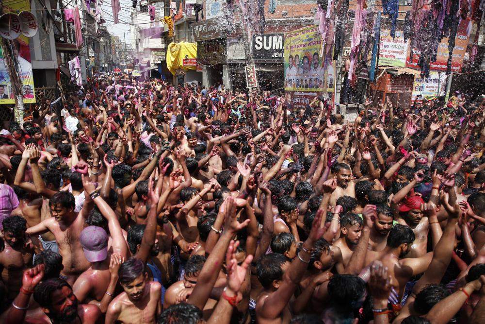 In this March 29, 2021, file photo, Indians, their faces smeared with color and glitter, dance as water is sprinkled on them during Holi celebrations in Prayagraj, India.