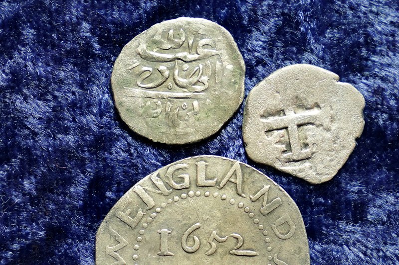 A 17th century Arabian silver coin, top, that research shows was struck in 1693 in Yemen, rests near an Oak Tree Shilling minted in 1652 by the Massachusetts Bay Colony, below, and a Spanish half real coin from 1727, right, on a table, in Warwick, R.I., Thursday, March 11, 2021. 
