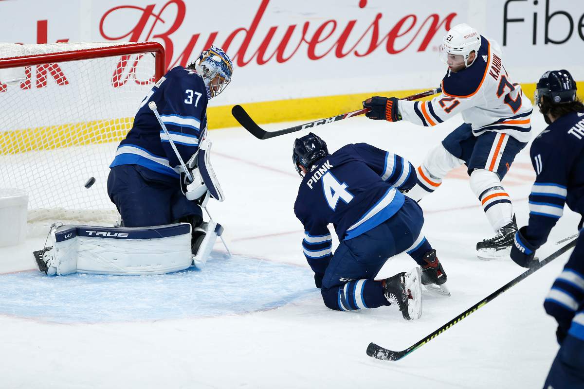 Winnipeg Jets goaltender Connor Hellebuyck (37) saves the shot from the Edmonton Oilers’ Dominik Kahun (21) as Neal Pionk (4) defends during second-period NHL action in Winnipeg on Saturday, April 17, 2021.
