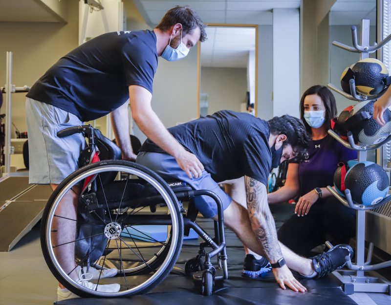 Humboldt Broncos bus crash survivor Ryan Straschnitzki, centre, is helped into his wheelchair by Eric Daigle, left, and Jill Mack while he attends a physiotherapy session in Calgary, Alta., Thursday, June 24, 2021.