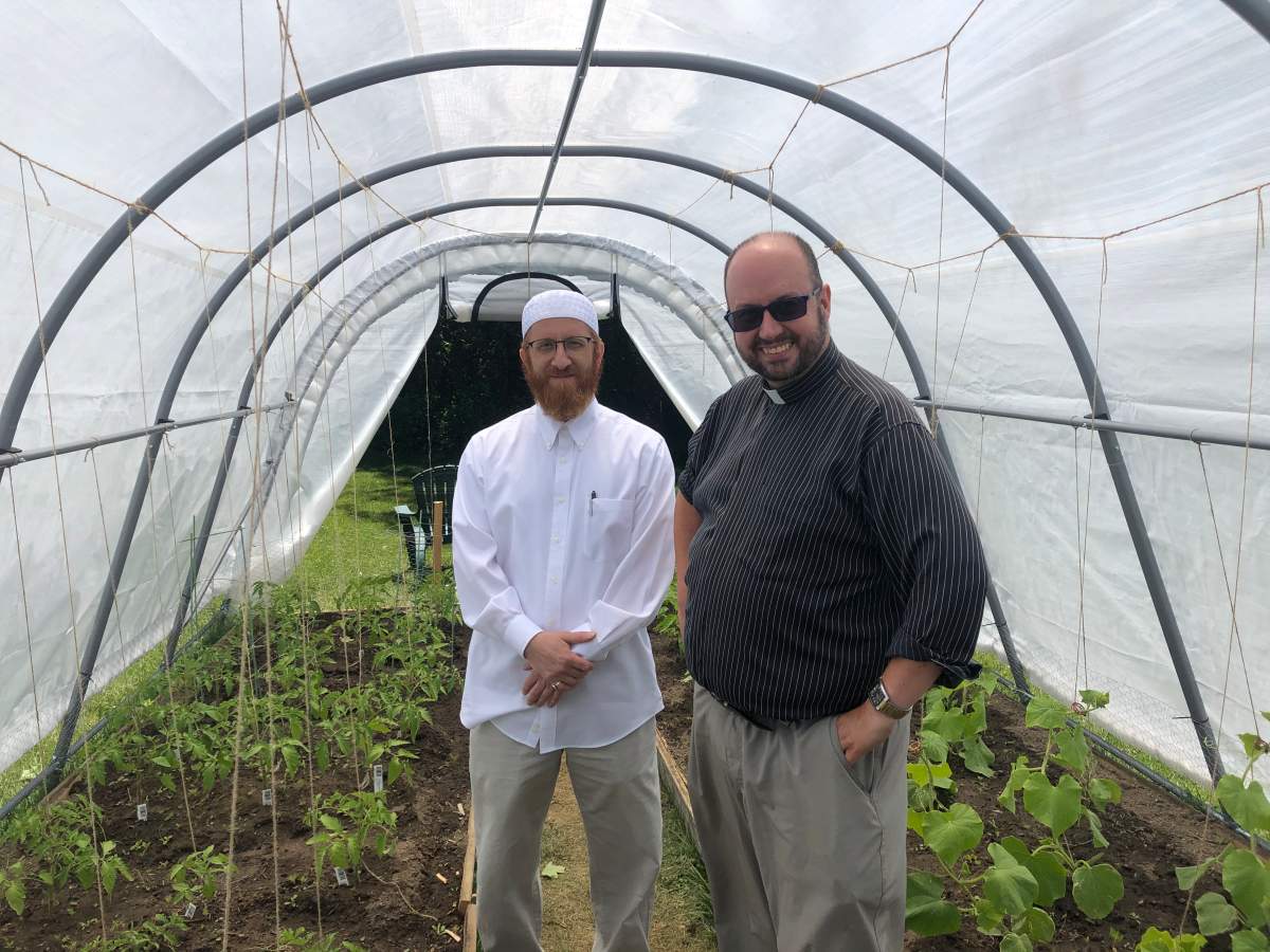 Imam Abd Alfatah Twakkal (left) of the London Muslim Mosque and Canon Kevin George stand inside Abraham’s Tent, an interfaith greenhouse at St. Aidan’s Anglican Church.