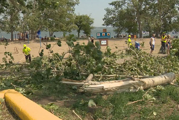 Crews pick up fallen branches and debris left on the beach following a storm Sunday night in Regina Beach. (Derek Putz / Global News)