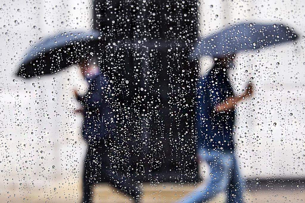 Raindrops form on a window as pedestrians shield from the rain with umbrellas.
