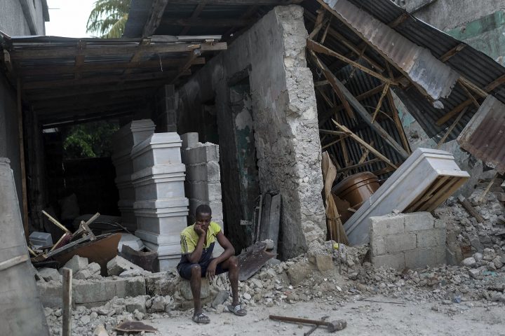 A man sits in front of a collapsed funeral home in Les Cayes, Haiti, Monday, Aug. 16, 2021