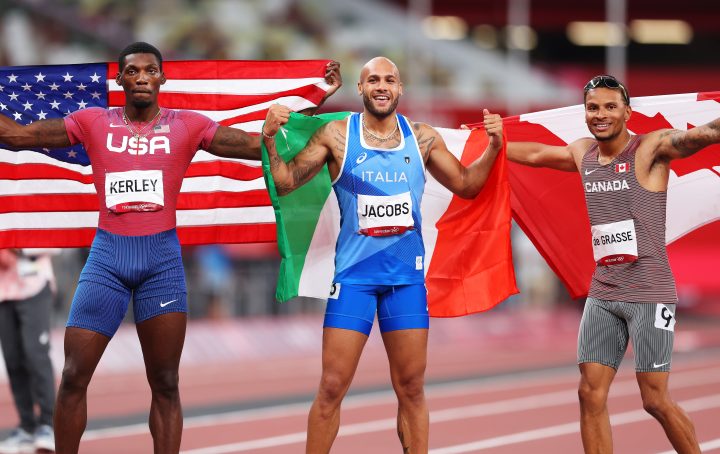 Bronze medalist Andre De Grasse of Team Canada, gold medalist Lamont Marcell Jacobs of Team Italy and silver medalist Fred Kerley of Team United States pose on the track following the Men’s 100m Final