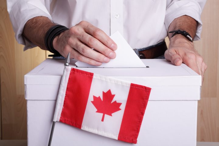 A man casting his vote. The Canadian flag is in front of the ballot box.