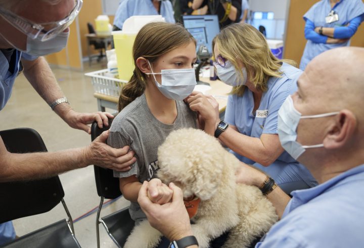 Mika-Ella Varin, 11, holds Bemol as she gets vaccinated during the first day of vaccination for children aged five- to 11-years old in Montreal, Wednesday, Nov. 24, 2021. A health care worker brought his dog Bemol to distract children during vaccination. THE CANADIAN PRESS/Paul Chiasson