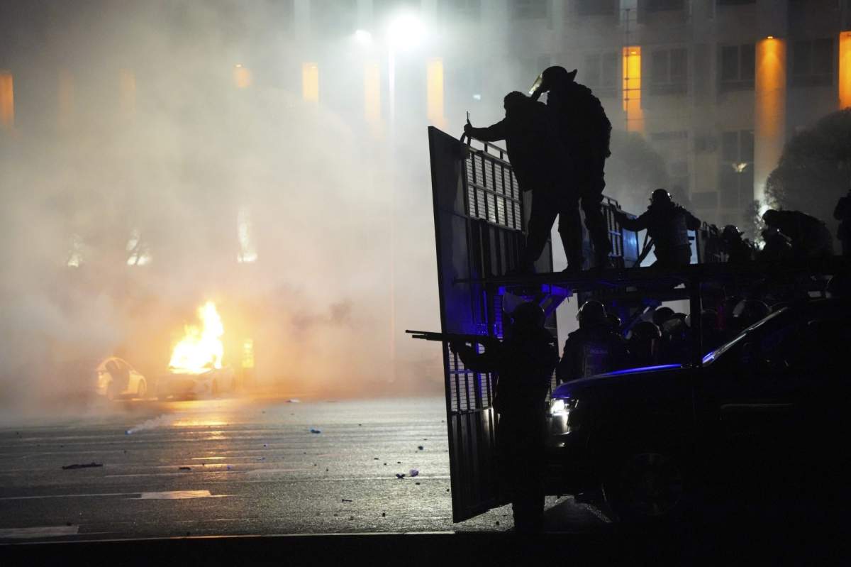 A police car on fire as riot police prepare to stop protesters in the center of Almaty, Kazakhstan, Wednesday, Jan. 5, 2022. Demonstrators denouncing the doubling of prices for liquefied gas have clashed with police in Kazakhstan's largest city and held protests in about a dozen other cities in the country. Local news reports said police dispersed a demonstration of about a thousand people Tuesday night in Almaty and that some demonstrators were detained. (AP Photo/Vladimir Tretyakov).