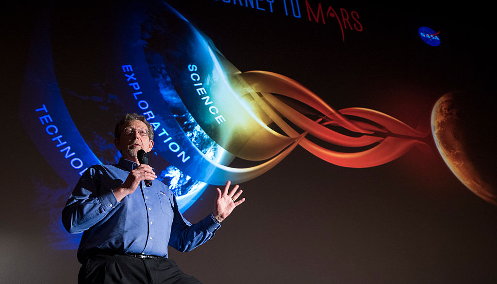 Jim Green speaks in from a screen with space graphics on it.
