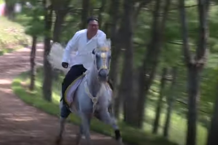 Kim Jong Un is seen on a white horse, riding through the woods