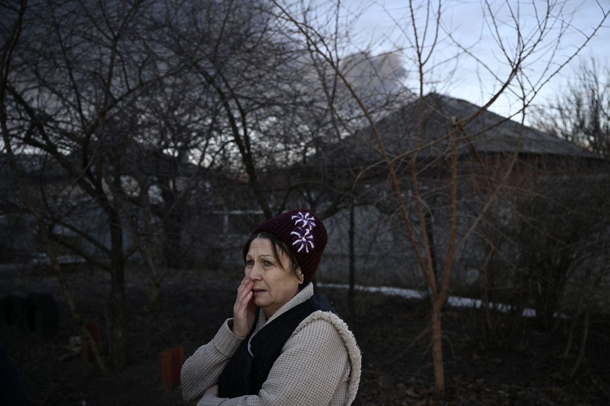 A woman stands in a street as black smoke rises from a military airport in Chuguyev near Kharkiv on February 24, 2022.