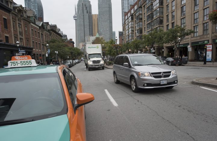 A ride sharing mini van (R) with an Uber sticker in the front window, drives past a parked Beck taxi, on Front St. East in downtown Toronto.