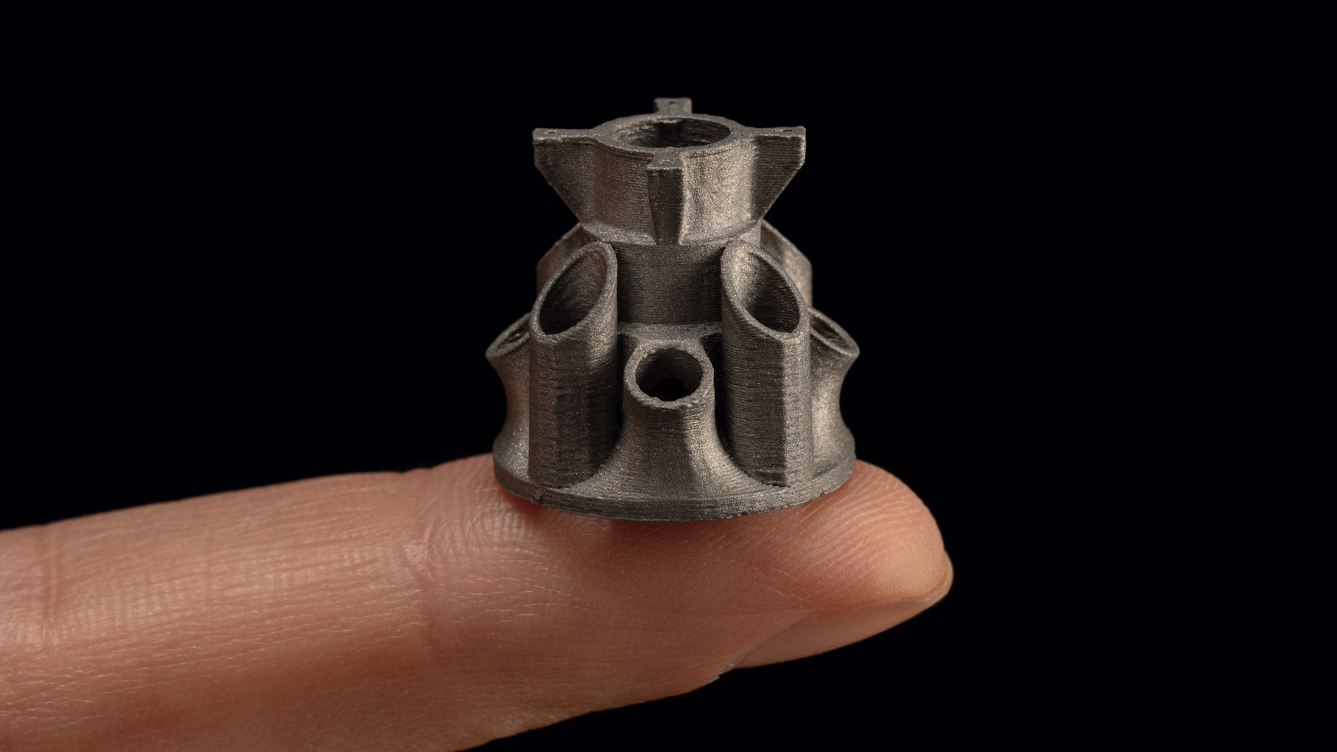 This photo shows an example of a tiny, but incredibly detailed 3D printed metal component made by Desktop Metal. In the photo, the individual print layers are clearly visible.