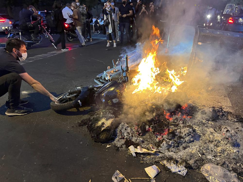 A man pulls out a police motorcycle which is set on fire during a protest over the death of a young woman who had been detained for violating the country's conservative dress code, in downtown Tehran, Iran.