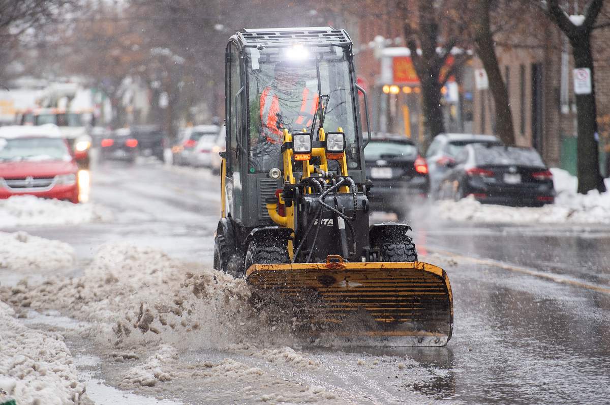 A plow clears water and slush from a street in Montreal, Friday, Dec. 23, 2022, as a storm system bears down on the region.