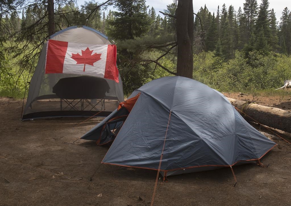 Campers with a Canadian flag flying on their camp site are shown in Algonquin Park on Saturday, June 12, 2021. Parks Canada says visitors will be able to start booking reservations for camping and other activities at its sites across the country in March. THE CANADIAN PRESS/Fred Thornhill.