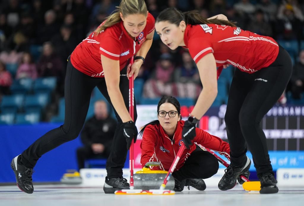 Team Canada skip Kerri Einarson delivers a rock as lead Briane Harris, left, and second Shannon Birchard, right, sweep while playing Nova Scotia in the playoffs at the Scotties Tournament of Hearts, in Kamloops, B.C., on Saturday, February 25, 2023. THE CANADIAN PRESS/Darryl Dyck