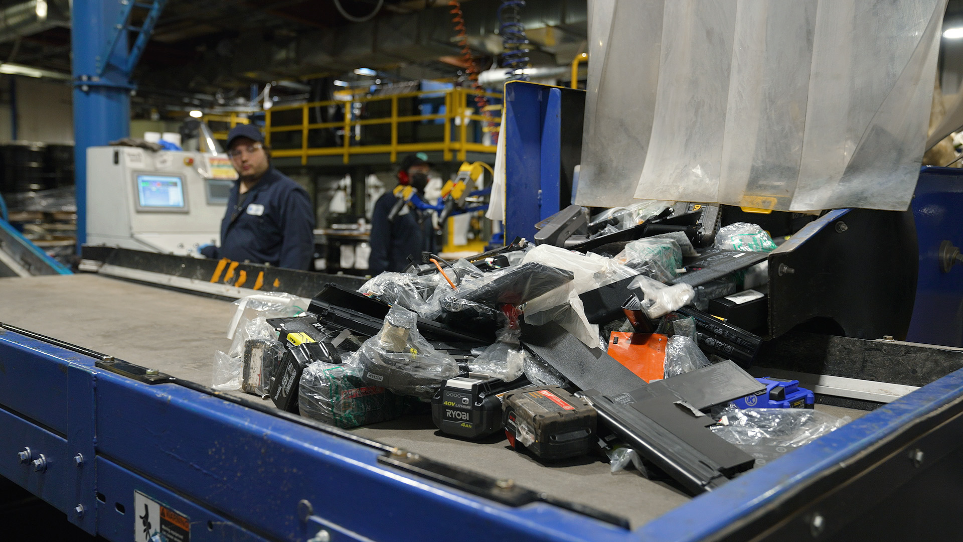 Drill, cellphone, and laptop batteries are dumped onto the conveyor at Li-Cycle's Kingston, ON plant. Each battery must be unwrapped and checked to make sure it is lithium-ion.
