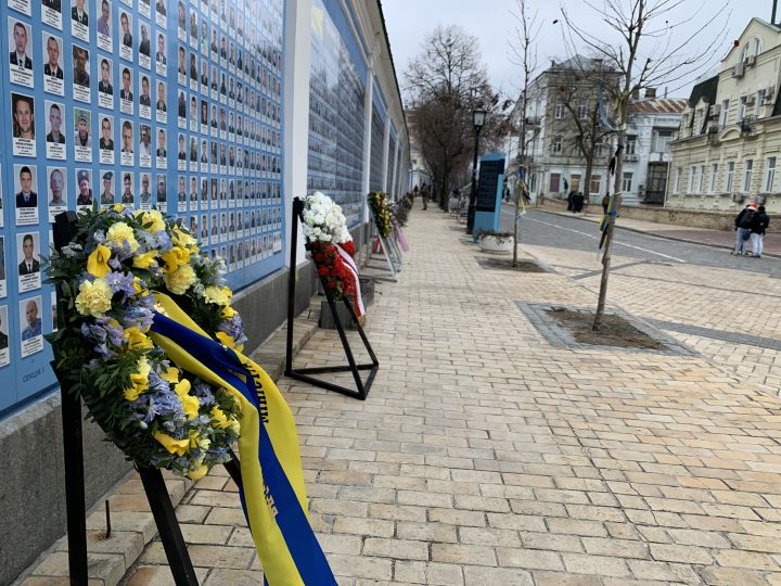 Wreaths and flowers adorn a wall covered with photos of soldiers killed during the war in Kyiv on Friday, Feb 24, 2023.