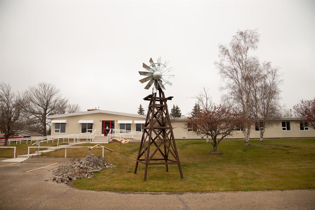 A large facility with beige siding and a ramp entrance has a small windmill out front.