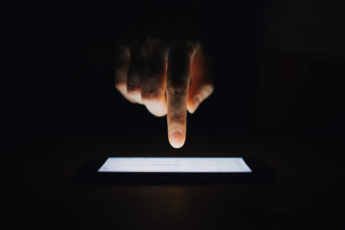 A hand over a cellphone. The background is dark.